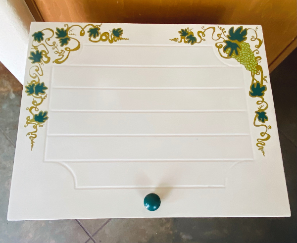 Can lid painted to look like a wooden door with a green knob and grapevines around the upper edges